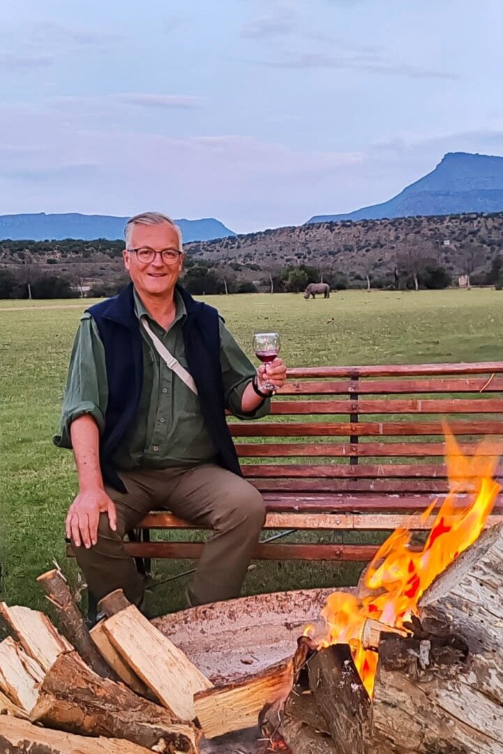 A guest with a glass of wine beside the campfire at dusk
