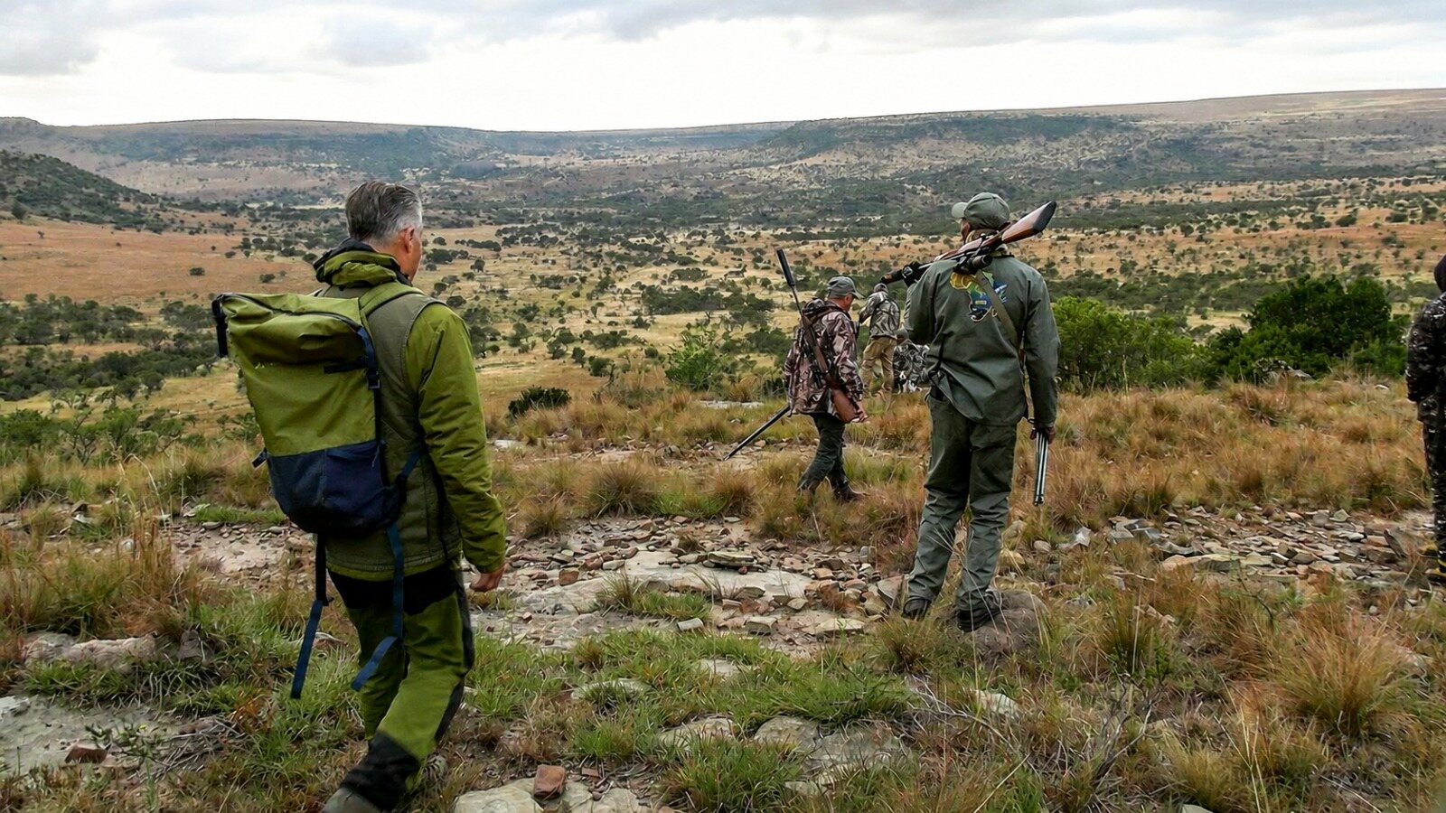 Hunters and guides crossing a rocky ridge above open bushveld
