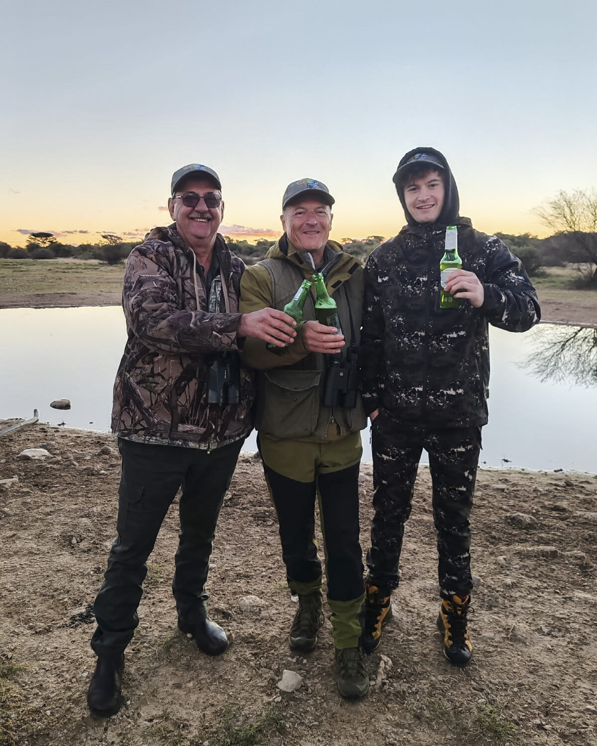 Three hunters in camouflage at a waterhole at sunset in South Africa