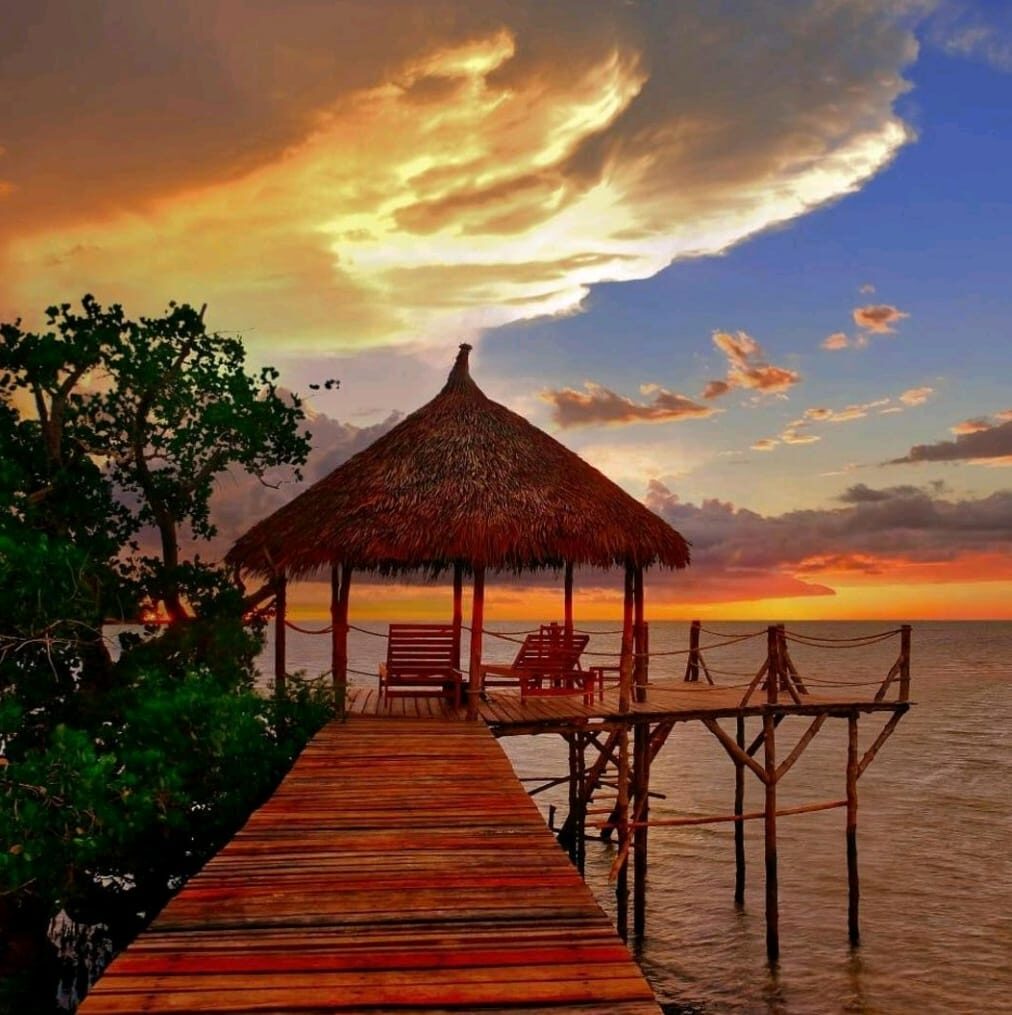 A wooden jetty and thatched gazebo over the sea at sunset on Nosy Be