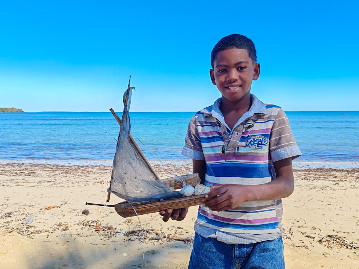 A boy on the beach holding a model sailing boat, Nosy Be