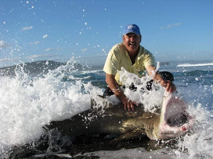 An angler landing a fish from the rocks as the surf breaks around him